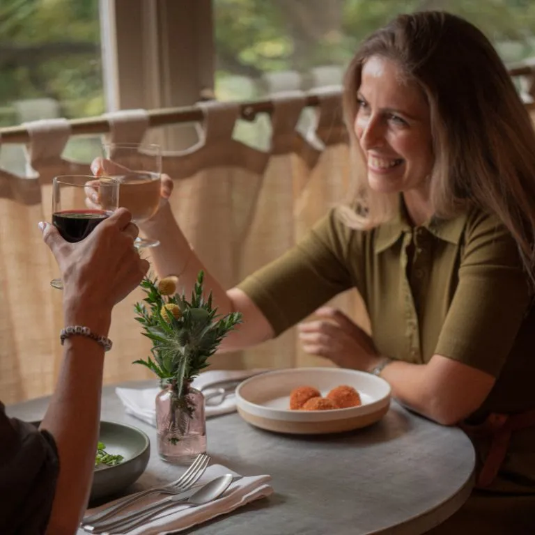 women smiling and cheersing a drink over 'nduja arancini