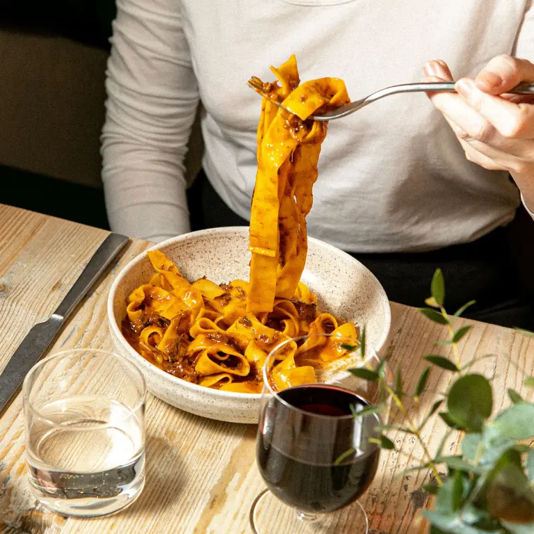 bowl of beef ragu next to a glass of wine