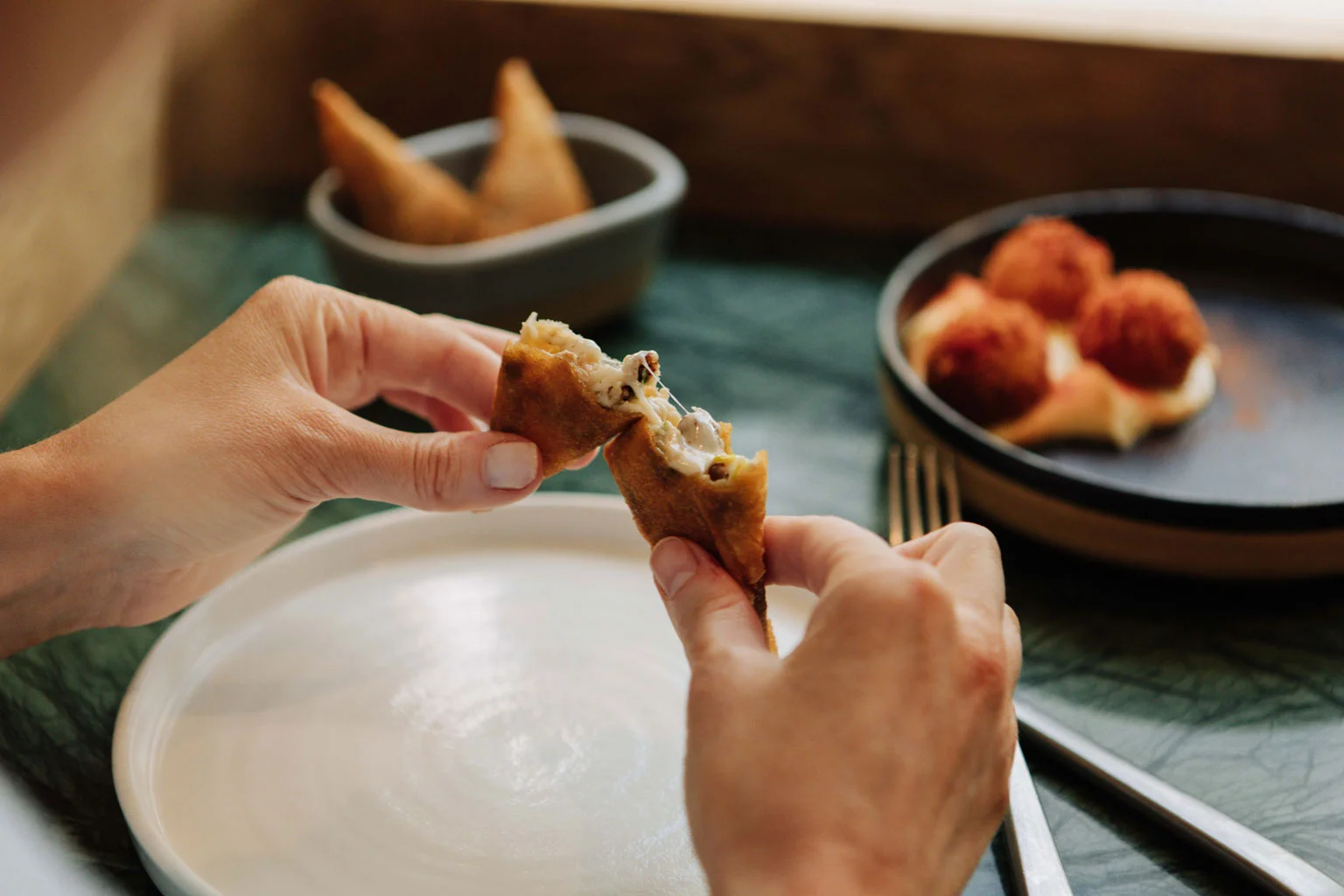 Photo of person breaking mortadella, ricotta & fior di latte torta fritta, with arancini in the background