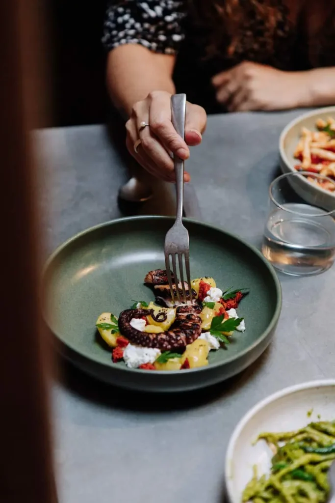 A person eating charred octopus salad, lemon dressed potato, ‘nduja & ricotta