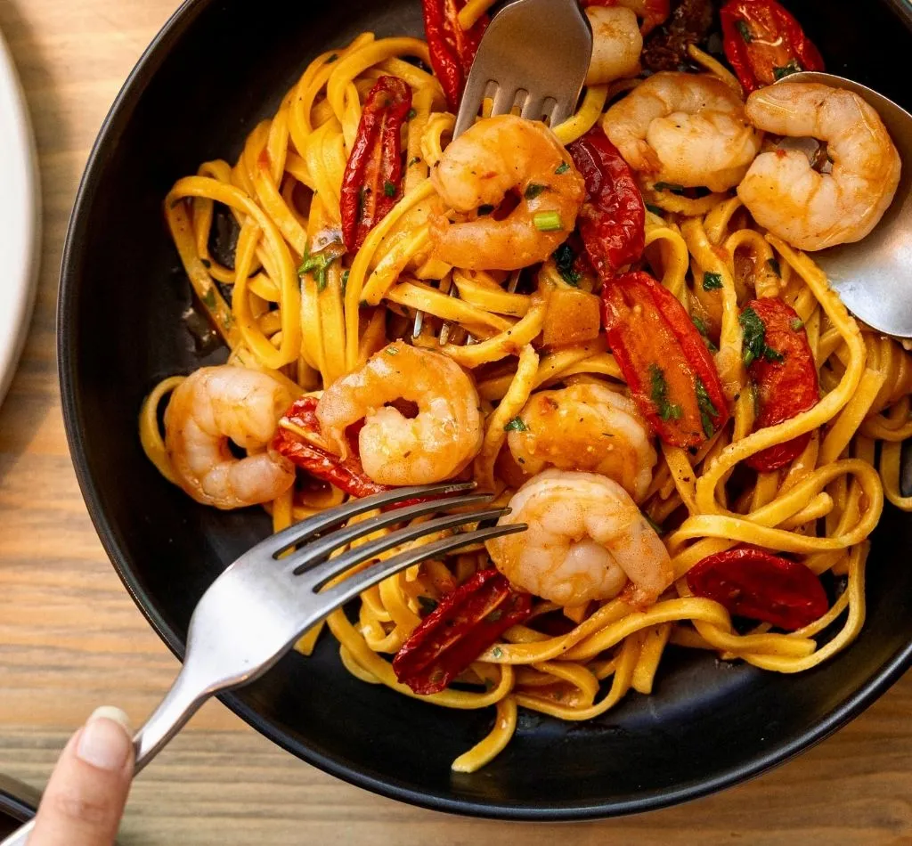 two forks and one spoon sharing a bowl of prawn linguine